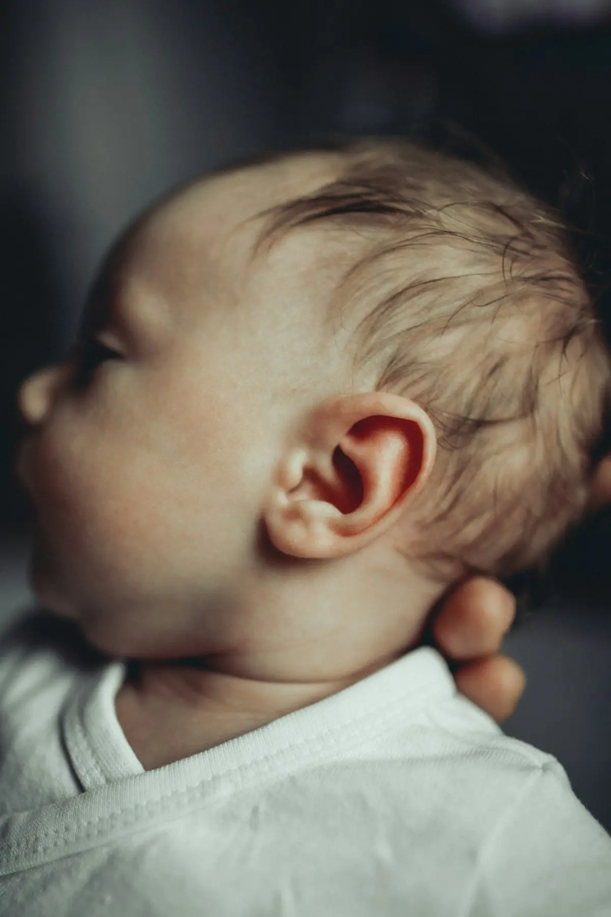 Perfil de un bebé en brazos, con la oreja en primer plano